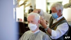 Un coiffeur portant un masque coupe les cheveux d'un client, également masqué, dans son salon de coiffure à Dortmund, en Allemagne, le 4 mai 2020. 