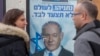 Dos personas conversan frente a un póster del primer ministro de Israel Benjamin Netanyahu, en un centro de votación en Hadera, en el norte de Israel. Diciembre 26 de 2019. Este día se celebraron las elecciones primarias del partido. AP/Ariel Schalit.