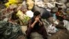FILE - Afghan refugees sit on sacks filled with used plastic items to sell at their makeshift shelter in a slum on the outskirt of Lahore, Jan. 12, 2015.